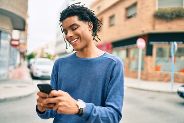 Fototapeta premium Young african american man smiling happy using smartphone at street of city.