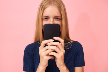 Blonde young female narrowing eyes, having suspicious look holding mobile, going to check messages of her unfaithful boyfriend. Teenage girl taking selfie using smart phone. People and gadgets