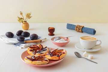 Small plum tarts on plate with cinnamon and icing sugar on white wooden table, delicious puff pastry dessert.