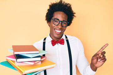 Handsome african american nerd man with afro hair holding books smiling happy pointing with hand and finger to the side