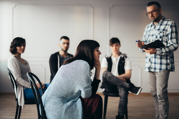 Handsome senior professional therapist stands in front of a group of people of different ages during meeting for people with social problems