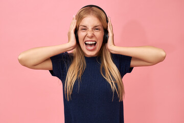 Portrait of beautiful young female with teeth brackets and blonde hair posing isolated in wireless headphones, screaming, listening to music via online streaming service, expressing genuine emotions