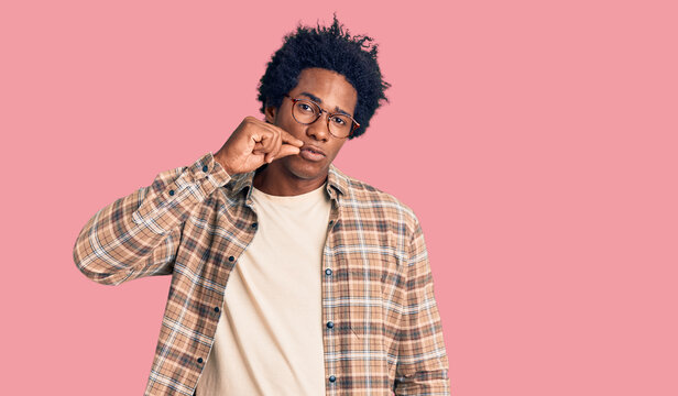 Handsome african american man with afro hair wearing casual clothes and glasses mouth and lips shut as zip with fingers. secret and silent, taboo talking