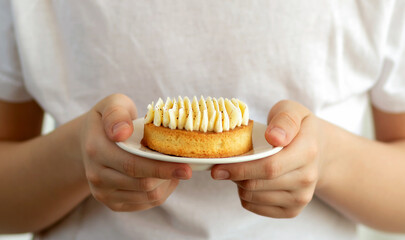 Selective focus to a child holding in hands a plate with vanilla cake.