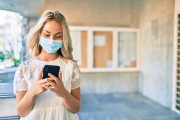 Young caucasian girl wearing medical mask using smartphone at street of city.