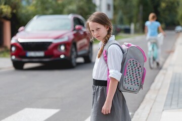 Pretty schoolgirl with pigtails and a pink - gray backpack is standing on one-way street
