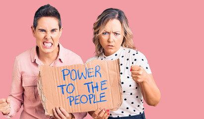 Couple of women holding power to the people banner annoyed and frustrated shouting with anger, yelling crazy with anger and hand raised