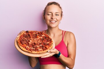 Beautiful caucasian woman holding italian pizza winking looking at the camera with sexy expression,...