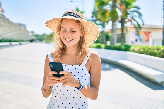 Young beautiful caucasian woman with blond hair smiling happy outdoors using smartphone