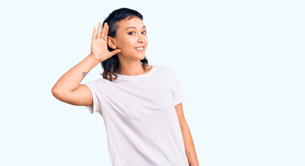 Young woman wearing casual clothes smiling with hand over ear listening an hearing to rumor or gossip. deafness concept.