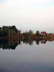 Fototapeta premium Autumn landscape with a lake surrounded by trees reflected in the water, against a blue sky. Rural landscape, a beautiful place to relax.