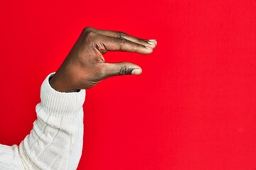 Fototapeta premium Arm and hand of african american black young man over red isolated background picking and taking invisible thing, holding object with fingers showing space