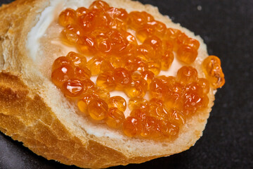 Macro shot of a mouthwatering sandwich with butter and red caviar on a black plate