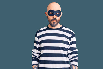 Obraz premium Young handsome man wearing burglar mask making fish face with lips, crazy and comical gesture. funny expression.