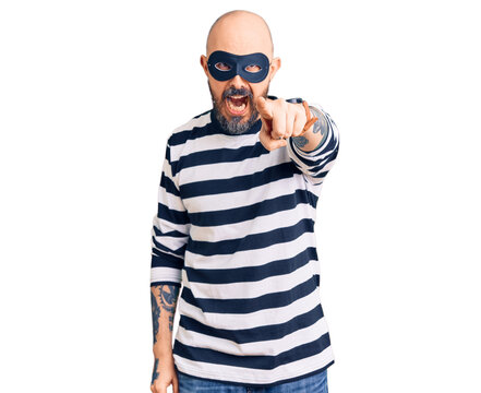 Young handsome man wearing burglar mask pointing displeased and frustrated to the camera, angry and furious with you