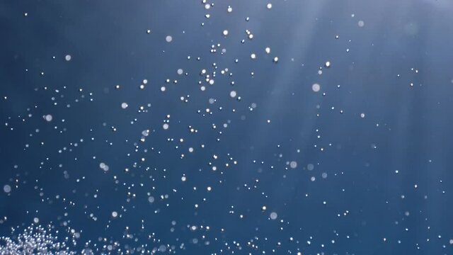 air bubbles underwater in blue water moving strange some in focus some out of focus making nive background shapes with sun rays and sun shine