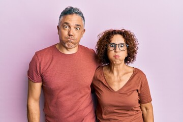 Fototapeta premium Beautiful middle age couple together wearing casual clothes puffing cheeks with funny face. mouth inflated with air, crazy expression.