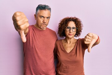 Beautiful middle age couple together wearing casual clothes looking unhappy and angry showing rejection and negative with thumbs down gesture. bad expression.