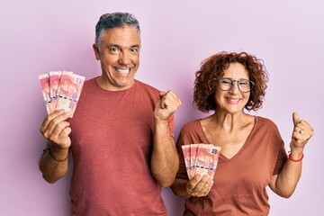 Beautiful middle age couple holding south african 50 rand banknotes screaming proud, celebrating...