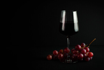 glass with red wine on a dark background and a bunch of red grapes.