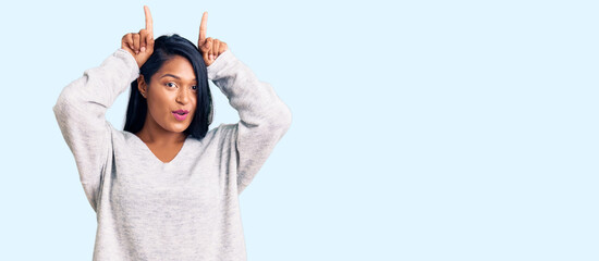 Hispanic woman with long hair wearing casual clothes doing funny gesture with finger over head as bull horns