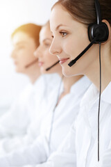 Call center. Beautiful young woman using headset and computer to help customers in sunny office. Business concept