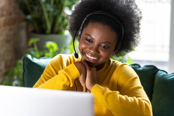 Smiling African American millennial woman wear headphones talk video calling, using laptop, teach...