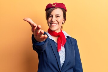Young beautiful woman wearing stewardess uniform smiling friendly offering handshake as greeting and welcoming. successful business.