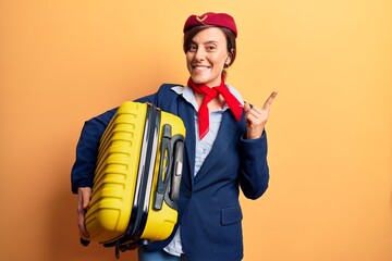 Young beautiful woman wearing stewardess uniform holding cabin bag smiling happy pointing with hand and finger to the side