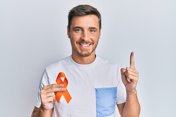 Handsome caucasian man holding awareness orange ribbon smiling with an idea or question pointing...