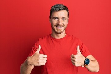 Handsome caucasian man wearing casual red tshirt success sign doing positive gesture with hand, thumbs up smiling and happy. cheerful expression and winner gesture.