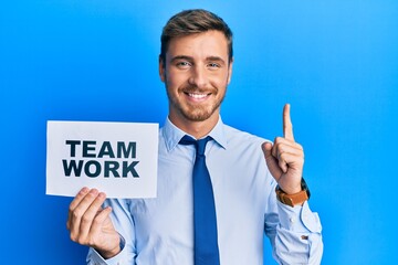 Handsome caucasian business man holding team work banner smiling with an idea or question pointing finger with happy face, number one