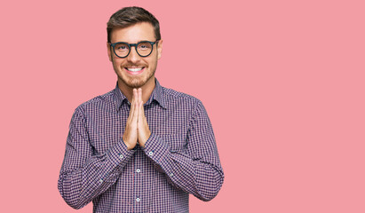 Handsome caucasian man wearing casual clothes and glasses praying with hands together asking for...