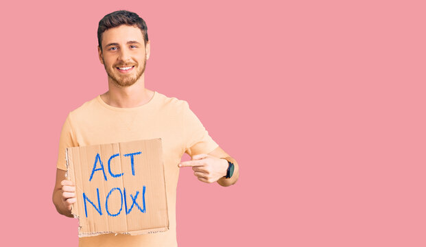 Handsome young man with bear holding act now banner smiling happy pointing with hand and finger