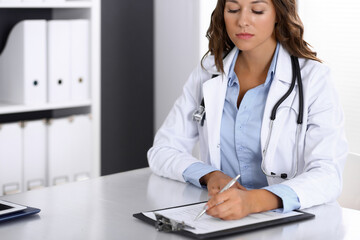 Doctor woman filling up medical form while sitting at the desk in hospital office. Physician at work. Medicine and health care concept