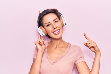 Fototapeta premium Young beautiful woman listening to music using headphones smiling happy pointing with hand and finger
