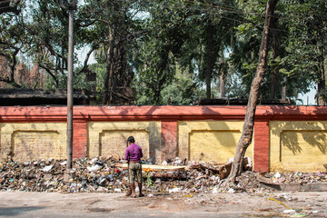 Fototapeta premium Kolkata, India - February 1, 2020: An unidentified man in purple shirt stands by himself with a broom infront of a big pile of plastic landfill waste on February 1, 2020 in Kolkata, India