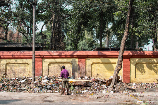 Kolkata, India - February 1, 2020: An unidentified man in purple shirt stands by himself with a broom infront of a big pile of plastic landfill waste on February 1, 2020 in Kolkata, India