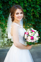 Happy bride in a long white wedding dress and veil in a green park on nature. Wedding image of a young girl, women's makeup and hairstyle. Marriage concept