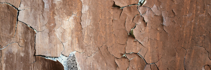 Peeling paint on the wall. Panorama of a concrete wall with old cracked flaking paint. Weathered rough painted surface with patterns of cracks and peeling. Grunge texture for wide panoramic background