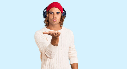 Young hispanic man listening to music using headphones looking at the camera blowing a kiss with hand on air being lovely and sexy. love expression.