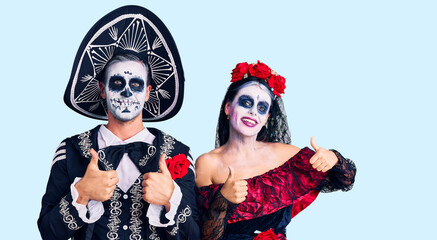 Young couple wearing mexican day of the dead costume over background success sign doing positive gesture with hand, thumbs up smiling and happy. cheerful expression and winner gesture.