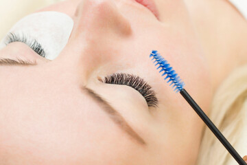 young woman is undergoing a close-up eyelash extension procedure. Eyelash brush