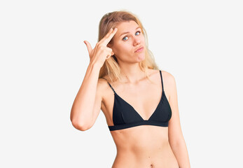 Young beautiful blonde woman wearing bikini shooting and killing oneself pointing hand and fingers to head like gun, suicide gesture.