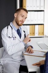 Friendly red-bearded doctor and patient woman discussing current health examination while sitting in sunny clinic. Medicine concept