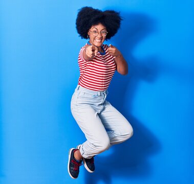 Young beautiful african american woman wearing casual clothes and glasses smiling happy. Jumping with smile on face over isolated blue background