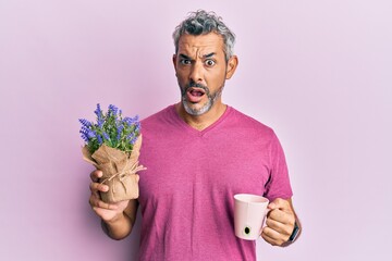 Middle age grey-haired man drinking a cup of infused lavender in shock face, looking skeptical and...