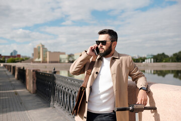 Bearded young businessman talking on smartphone while standing by riverside