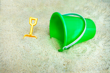 plastic green beach bucket with white hangle and yellow little hand shovel on sandy beach of sandbox © Mirror-images
