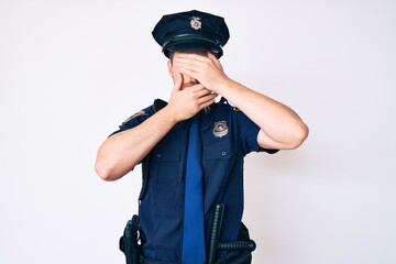 Young caucasian man wearing police uniform covering eyes and mouth with hands, surprised and shocked. hiding emotion